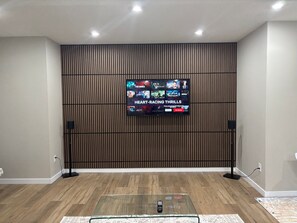 Ein modernes Wohnzimmer mit einem Flachbildfernseher an einer Wand aus Holzpaneelen, einem Glastisch und einem gemusterten Teppich.