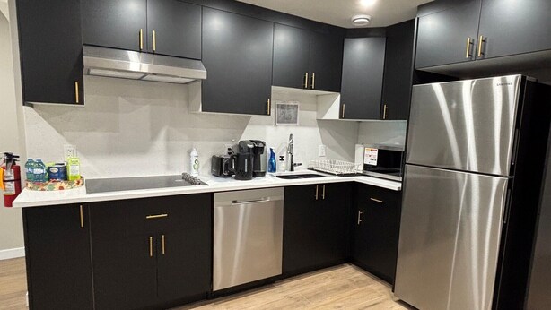A modern kitchen with black cabinets, stainless steel appliances, and a wooden floor. - 10 minutes from the YYC airport! Modern basement suite with all facilities (Calgary)
