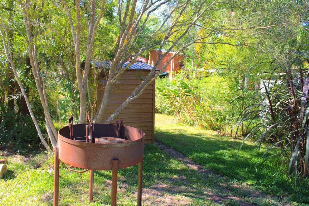 Una parrilla metálica con chimenea, rodeada de árboles y una estructura de madera en un jardín.