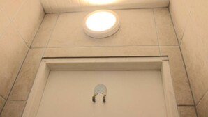 Une salle de bain avec des toilettes blanches, un luminaire rond placé au-dessus des toilettes et un petit miroir.