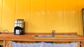 Une cuisine avec une machine à café en acier inoxydable posée sur un comptoir en bois, un évier et un rideau blanc en dentelle.