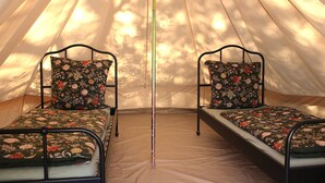 Une tente équipée de deux lits, chacun agrémenté de draps à motifs floraux et doté d’un cadre en métal.
