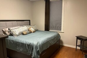 A bedroom with a bed, a window with blinds, a nightstand, and a small table. - Cozy Updated 2BR Home Near Carondelet Park (St. Louis)
