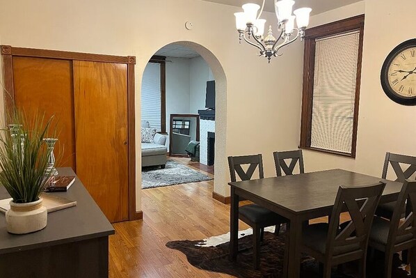 A dining area with a table and chairs, a chandelier, and a clock on the wall. - Cozy Updated 2BR Home Near Carondelet Park (St. Louis)