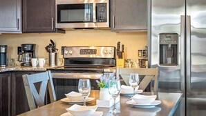 A modern kitchen with stainless steel appliances, a dining table set for four, and a microwave above the stove. - Private Retreat w/ Hot Tub, Pool Table, & Scenic Views (Sevierville)