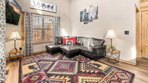 A living room with a black leather sofa, patterned rug, and artwork on the walls. - Private Retreat w/ Hot Tub, Pool Table, & Scenic Views (Sevierville)