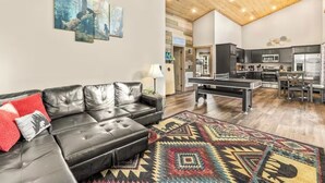 A modern living room with a leather sofa, a pool table, and a kitchen in the background. - Private Retreat w/ Hot Tub, Pool Table, & Scenic Views (Sevierville)