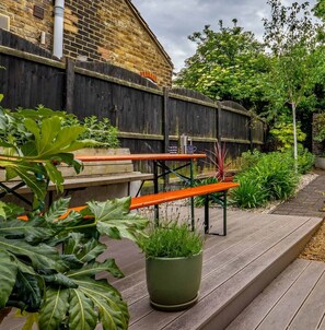 A wooden deck with benches, a potted plant, and a brick wall. - Seagrass Cottage - Perfect holiday cottage with parking in Whitstable. Sleeps 6 (Kent)