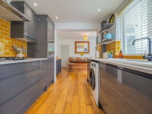 A modern kitchen with grey cabinets, a washing machine, and a dining area with a table and chairs. - Seagrass Cottage - Perfect holiday cottage with parking in Whitstable. Sleeps 6 (Kent)