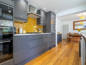 A modern kitchen with grey cabinetry, a brick backsplash, and a wooden floor. - Seagrass Cottage - Perfect holiday cottage with parking in Whitstable. Sleeps 6 (Kent)
