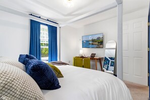 Un dormitorio con una cama, un escritorio con una computadora portátil, un cuadro y un espejo en la pared.