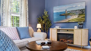 A living room with a sofa, coffee table, fireplace, and a painting of a coastal scene. - Wells Retreat: 3BR, Firepit, Pickleball, Sleeps 9 (Wells)