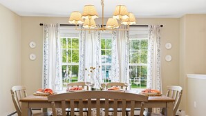 A dining room with a wooden table and chairs, a chandelier, and patterned curtains. - Wells Retreat: 3BR, Firepit, Pickleball, Sleeps 9 (Wells)