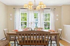 Un comedor con mesa y sillas de madera, una araña y cortinas estampadas.