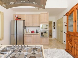 A modern kitchen with a gas stove, stainless steel appliances, wooden cabinets, and a wooden cabinet with glass doors. - La Sorgente by Interhome (Saturnia)