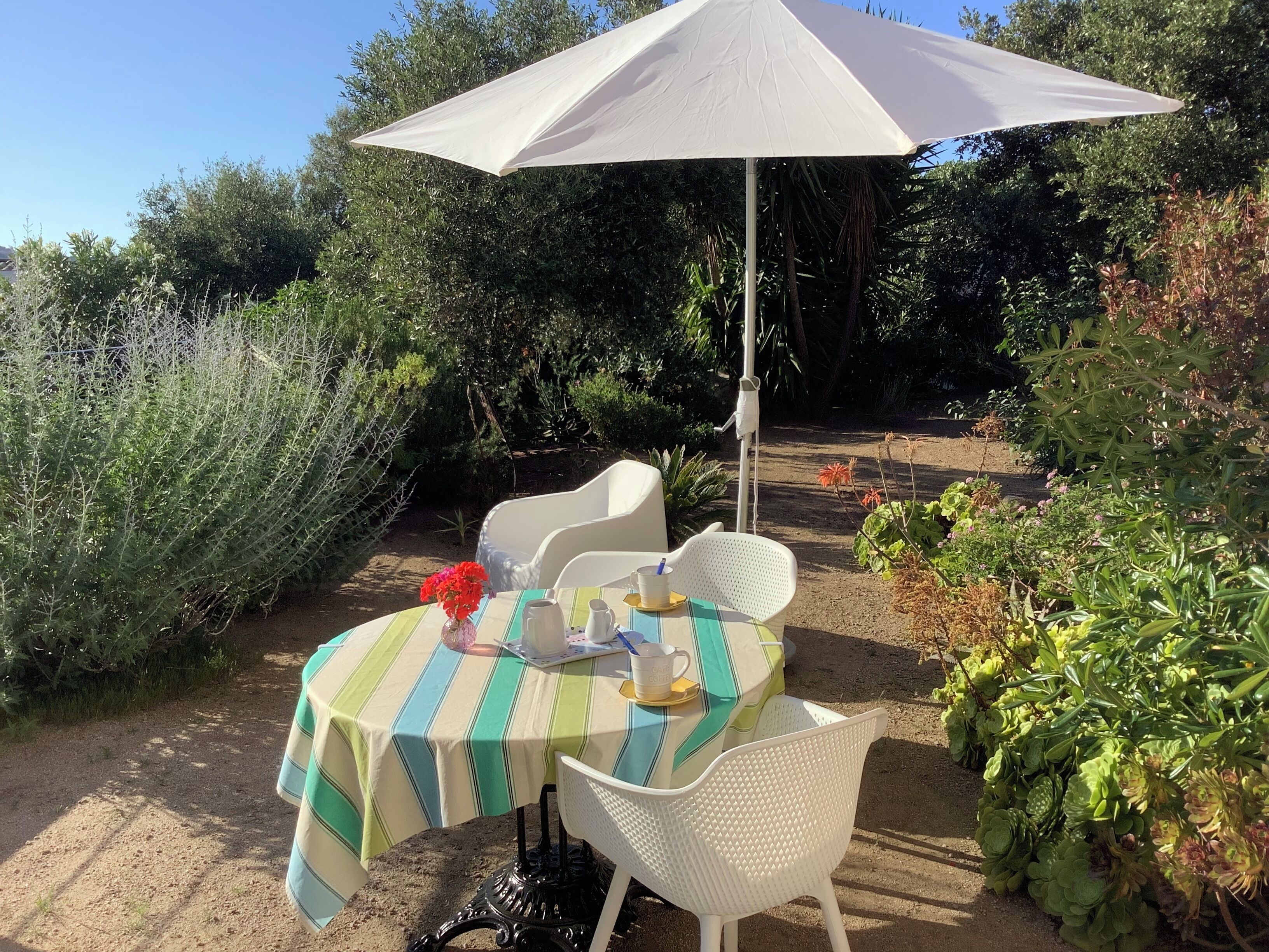 An outdoor table with a striped tablecloth, white chairs, and a white umbrella.