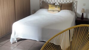 Een slaapkamer met een bed, een houten garderobe, een gele stoel en een nachtkastje met een lamp.