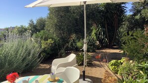 Een buiten eethoek met een tafel voor twee, omgeven door groen en een witte parasol.