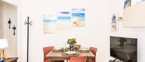 Uma sala de jantar com mesa posta para quatro pessoas, televisão e obras de arte na parede.