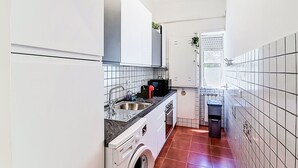 Eine kleine Küche mit Waschmaschine, Spüle und Fenster.