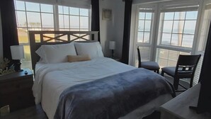 A hotel room with a bed, a chair, a desk, and large windows. - Sun Filled Corner Unit w/ Gulf Views in Every Room, Steps Away from Babe's Beach (Galveston)