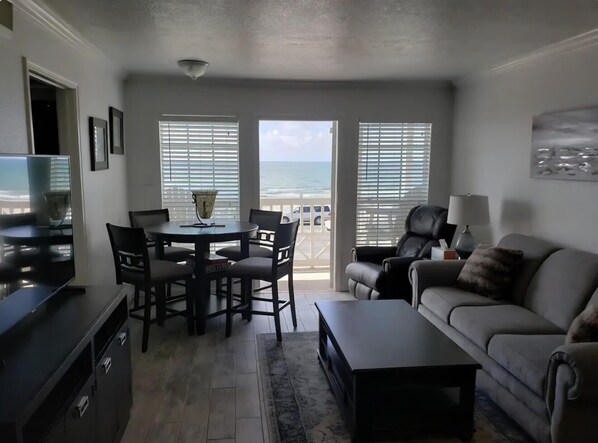 Ein Wohnzimmer mit Balkon, einem Esstisch mit Stühlen, einer Couch, einem Fernseher und einer Lampe.