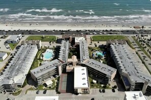 Eine Luftaufnahme eines Küstenhotels mit mehreren Gebäuden, einem zentralen Pool und einem Strand im Hintergrund.