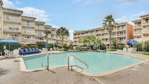 A swimming pool surrounded by lounge chairs and umbrellas, with a multi-story building in the background. - Sun Filled Corner Unit w/ Gulf Views in Every Room, Steps Away from Babe's Beach (Galveston)