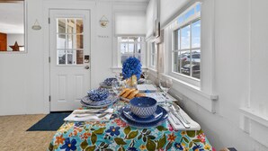 A dining room with a long table set for a meal, white walls, and large windows.