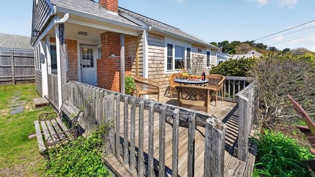 A house with a wooden deck, a brick chimney, and a porch with wicker furniture.