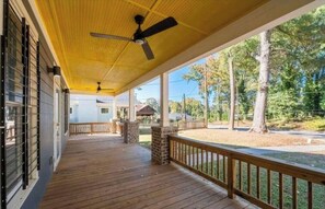 A covered porch with a ceiling fan, wooden flooring, and a view of trees and a building in the background. - Spacious 4 br 3 ba! Minutes to Benz stadium, airport, downtown, and AU Center. (Atlanta)