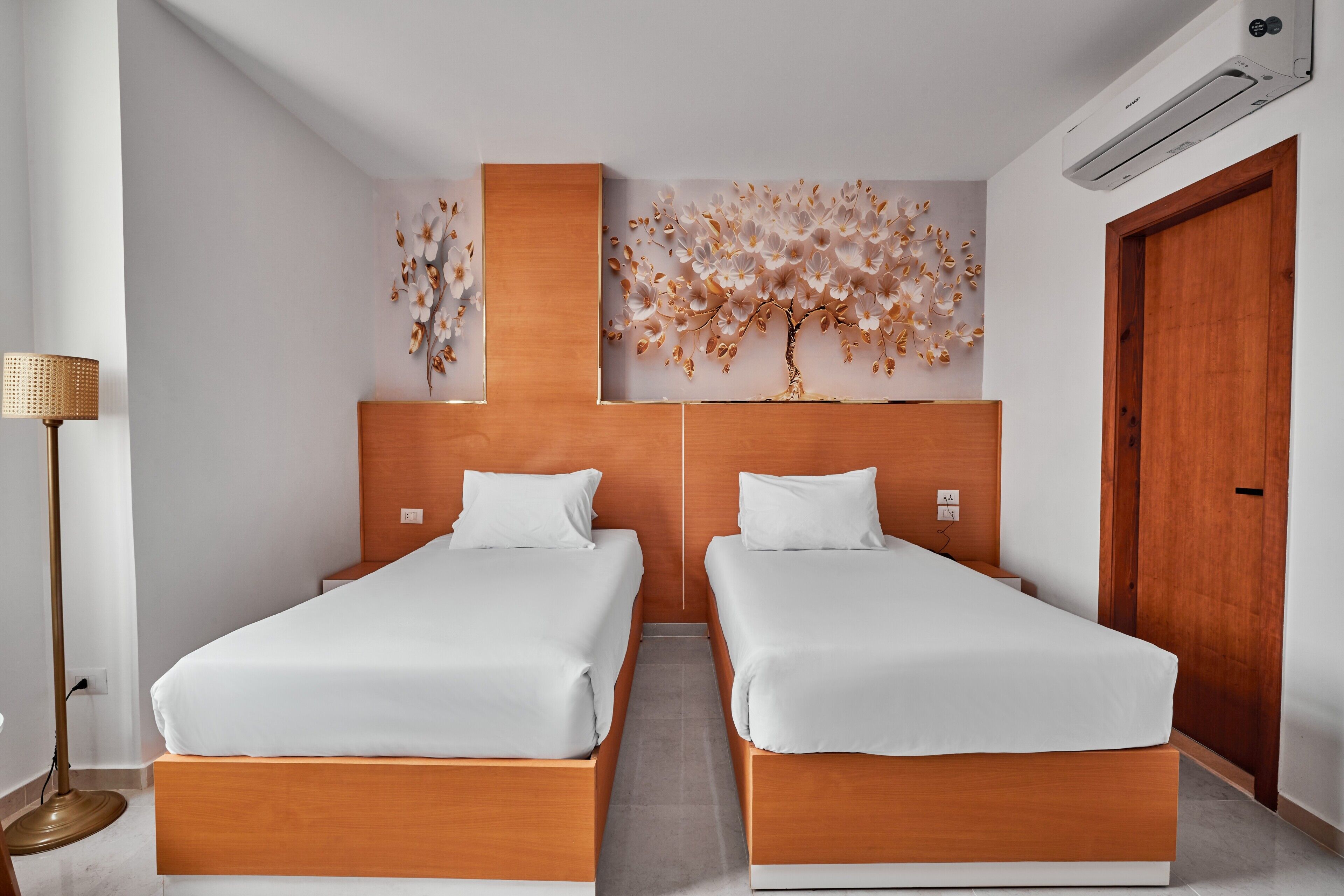 Habitación de hotel con dos camas, aire acondicionado de pared y una lámpara de pie.