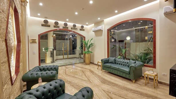 A lobby with a green sofa, a large potted plant, and a marble floor.