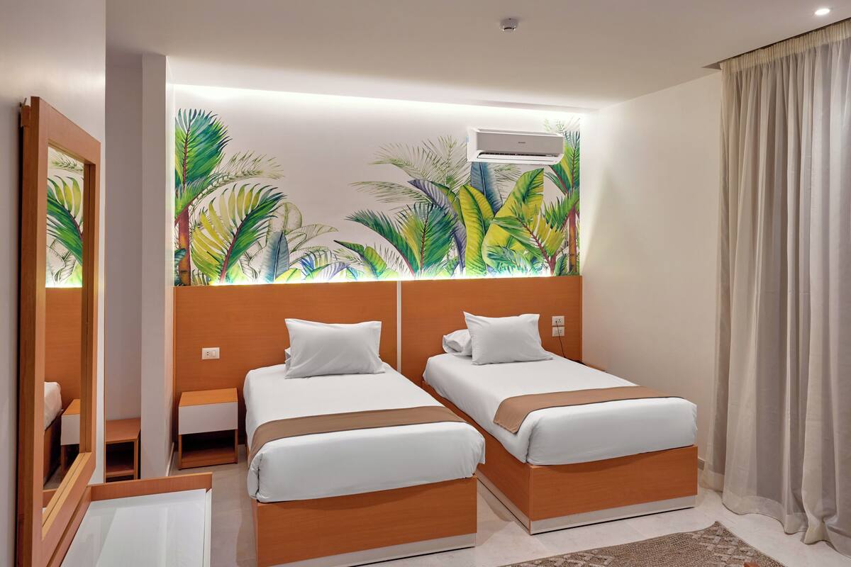 A hotel room with two beds, a large mirror, an air conditioning unit, and a tropical-themed mural on the wall.