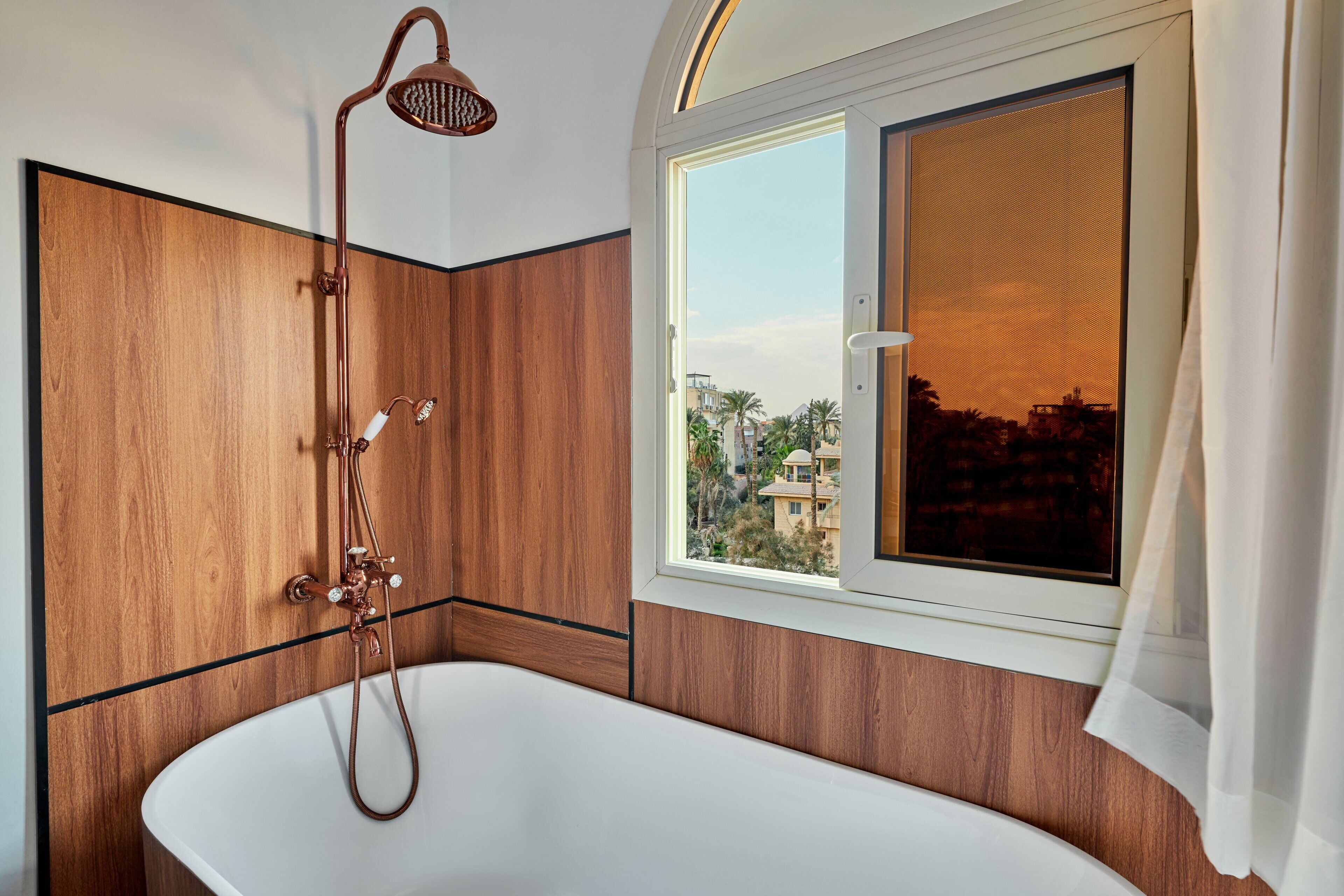 A bathroom with a freestanding bathtub, a showerhead, and a window with a view of buildings.