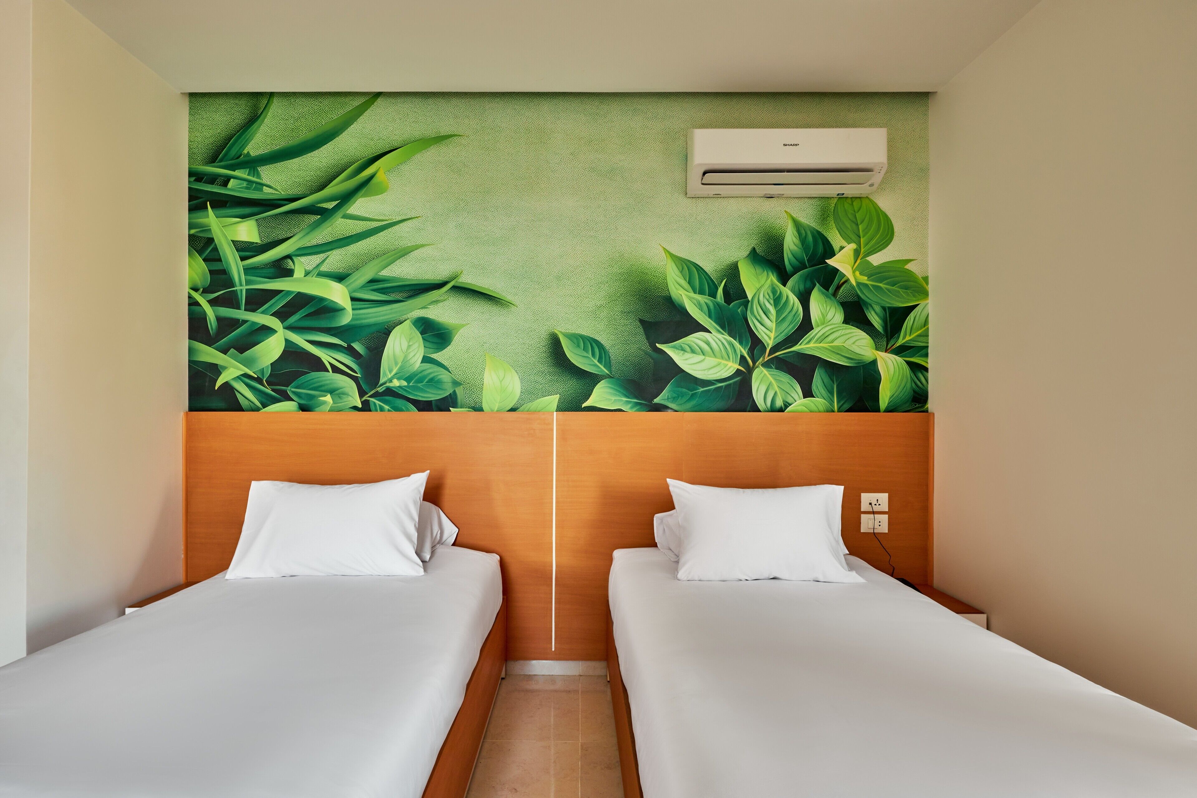 A hotel room with two beds, a green leaf mural on the wall, and an air conditioning unit.