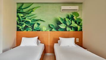 A hotel room with two beds, a green leaf mural on the wall, and an air conditioning unit.