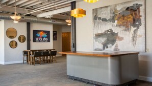 A modern reception area with a counter, wooden chairs, a table, and a large abstract painting on the wall. - The Hostel KC  (Kansas City)