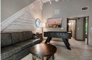 Ein Loft-Wohnzimmer mit holzverkleideter Schräge, einer Couch, einem Kicker, einer Lampe und einem Gemälde an der Wand.