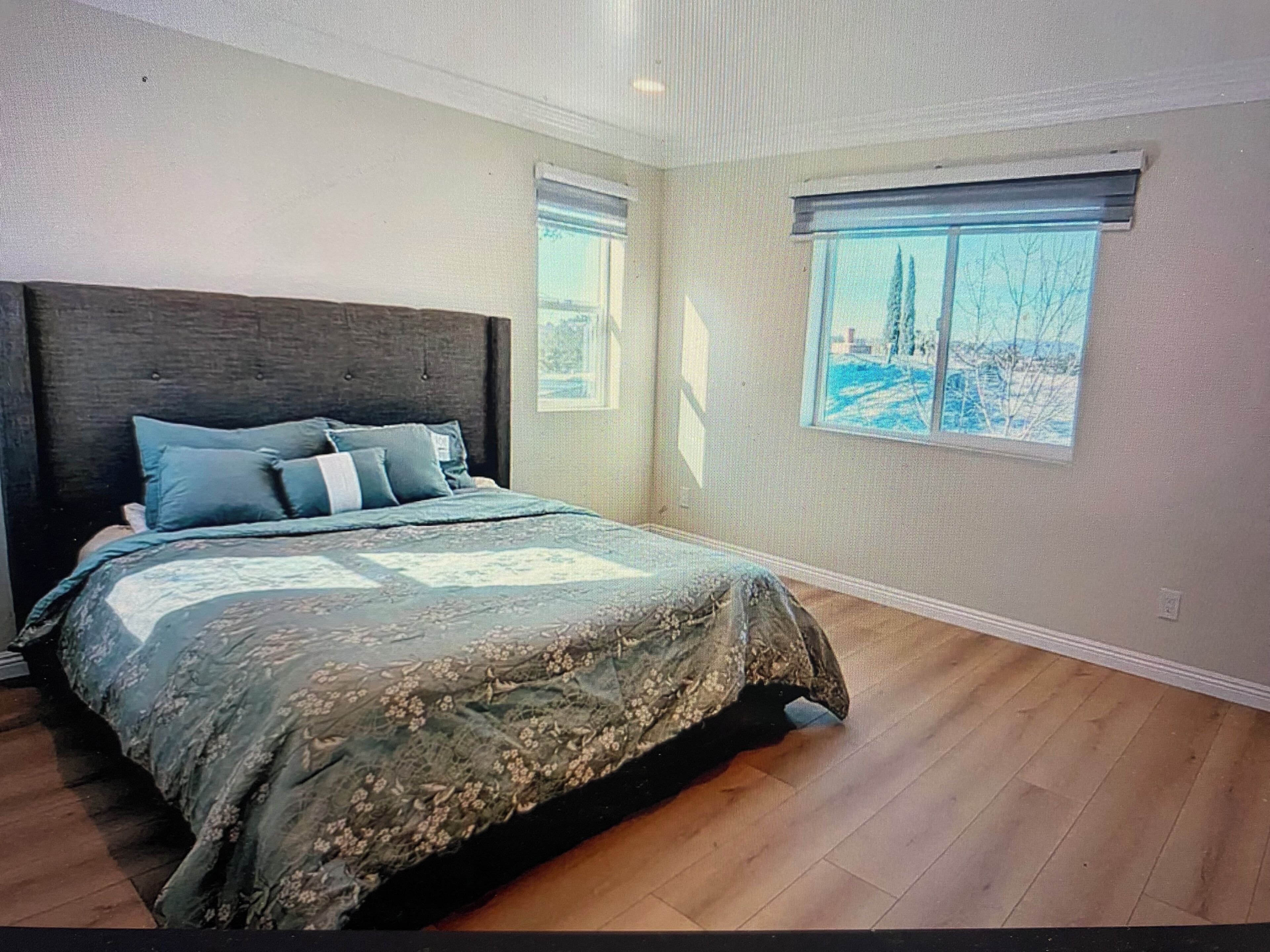 Quarto com uma cama grande, duas janelas e vista para árvores.
