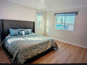 Ein Schlafzimmer mit einem großen Bett, zwei Fenstern und Blick auf Bäume.