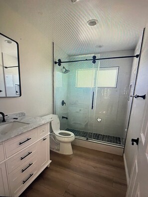 Ein Badezimmer mit Duschkabine, Toilette, Waschbecken mit Marmorplatte und Spiegel über dem Waschbecken.