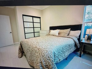 Ein Schlafzimmer mit einem Bett, einem Nachttisch, einem Fenster und einer Tür.