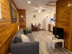 Una habitación acogedora con sofá, una mesa de comedor con sillas, un televisor sobre un mueble bajo y un ventilador de techo.