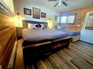 Quarto com cama, mesas de cabeceira, ventilador de teto e paredes de madeira.