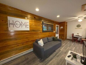 Uma sala de estar com parede de madeira, um sofá, uma mesa de jantar com cadeiras e um letreiro que diz 'HOME'.