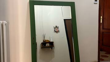 Una habitación con un espejo de marco verde, un radiador, un estante pequeño con adornos y una puerta de madera.