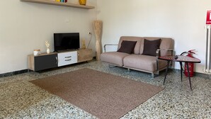 A living room with a sofa, TV, wooden cabinet, and a small table with a fire extinguisher. - Residence Corso Roma in the heart of Montecatini Terme (Montecatini Terme)