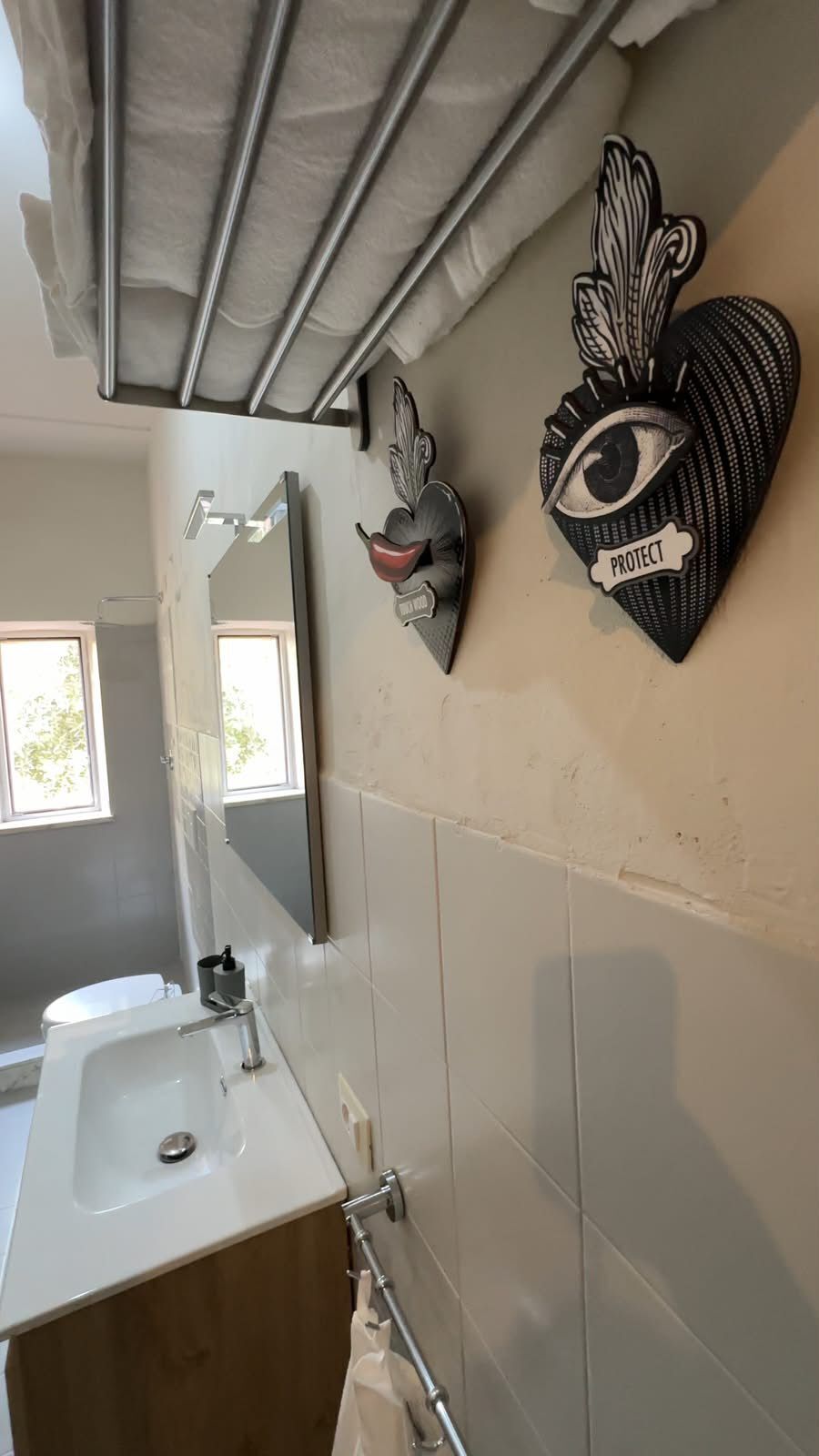 A bathroom with a white sink, a mirror, and two decorative wall pieces.