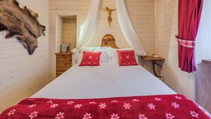A room with a bed, a wooden headboard, a wall-mounted crucifix, a fur rug, and a curtain.